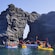 Kayakers raising their paddles in triumph by a natural rock formation in Cartagena, Spain